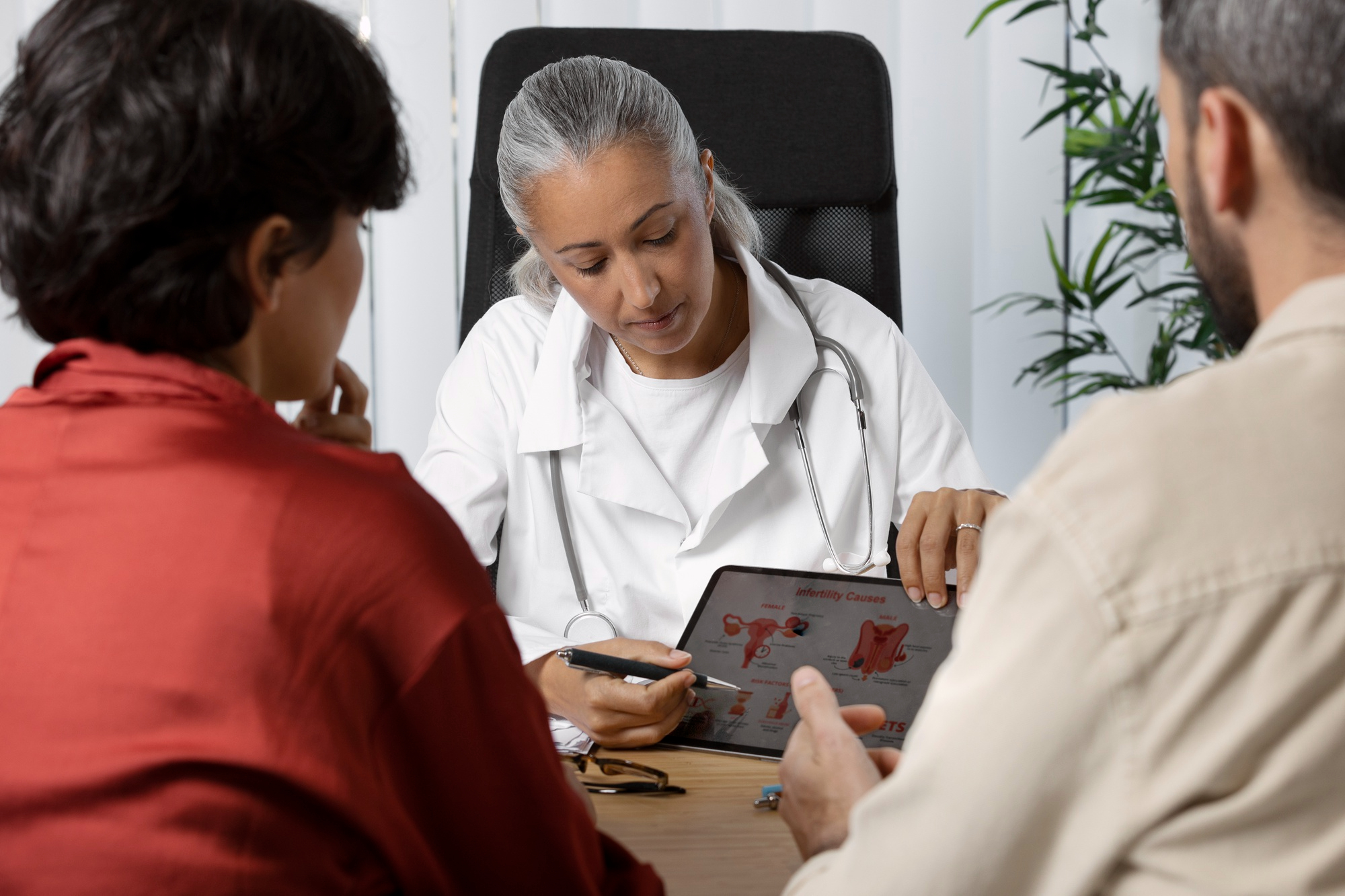 Doctora con pacientes con una tableta en mano con un diagrama que lee "causas de infertilidad"